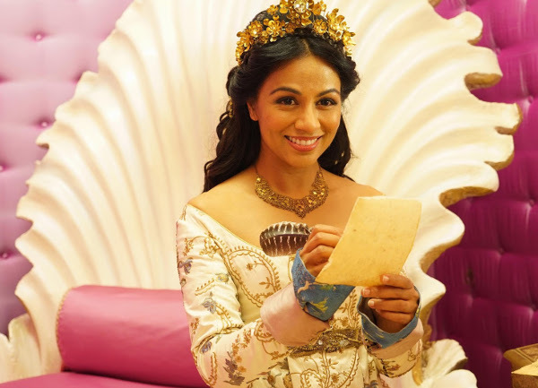 Karen David in costume, writing a letter.